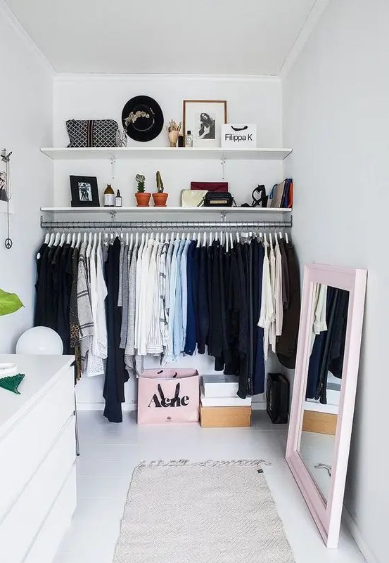 a neutral closet with a large rack, wall-mounted shelves, a white IKEa dresser, a mirror in a pink frame and some decor