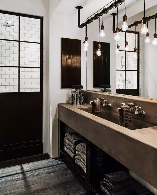 an industrial chic bathroom with a glazed shower space, a concrete vanity with a double sink, a rough wooden floor, exposed pipes and bulbs