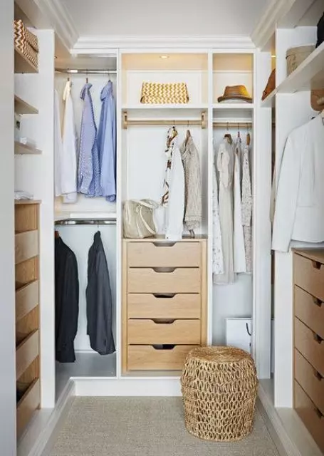 a small and cute closet with built in shelves, drawers, built in lights and a woven pouf plus racks for clothes
