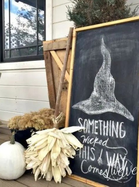 farmhouse Halloween decor with a chalkboard, a broom of husks, dried blooms and a white pumpkin is very cozy