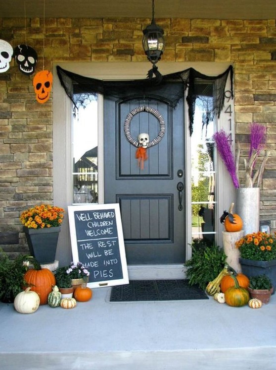 a whimsy and original Halloween porchh with skulls of paper, a skull wreath, a chalkboard sign, natural pumpkins and bold fall blooms