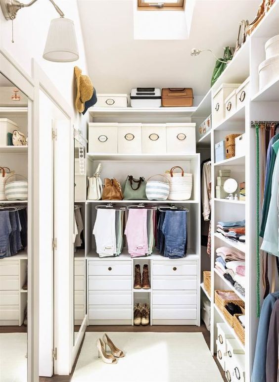 a small and stylish white closet with built-in shelves and drawers, boxes for shoes and hats and a large mirror on the wall