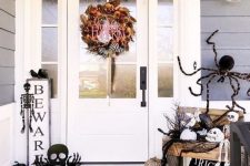 17 a black and white Halloween porch with a bright wreath, a small sign, a black bunting, skeletons and skulls, natural and faux pumpkins