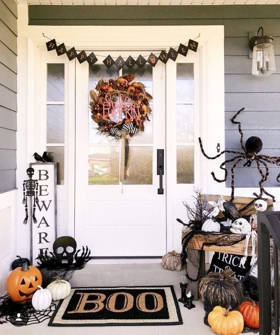 a black and white Halloween porch with a bright wreath, a small sign, a black bunting, skeletons and skulls, natural and faux pumpkins