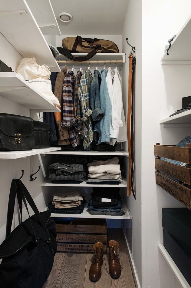 a small closet with wall mounted and built in shelves, a rack for hanging clothes, some crate drawers and boxes for shoes