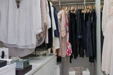 19 a small contemporary closet in white, with a large open shelf with boxes, dressers, holders with hangers and a stool