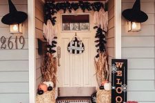 20 a bold Halloween porch with hay, orange, white and black pumpkins, bold blooms, corn husks, witches’ hats and evergreens