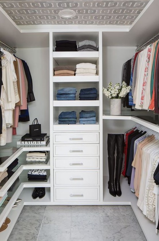 a small contemporary closet with open shelves, drawers, holders for hangers, glass shelves and a wallpaper ceiling