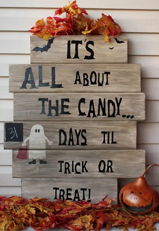 a chic pallet sign with black letters, a painted ghost and faux fall leaves is a fun and cool idea for Halloween with a rustic feel