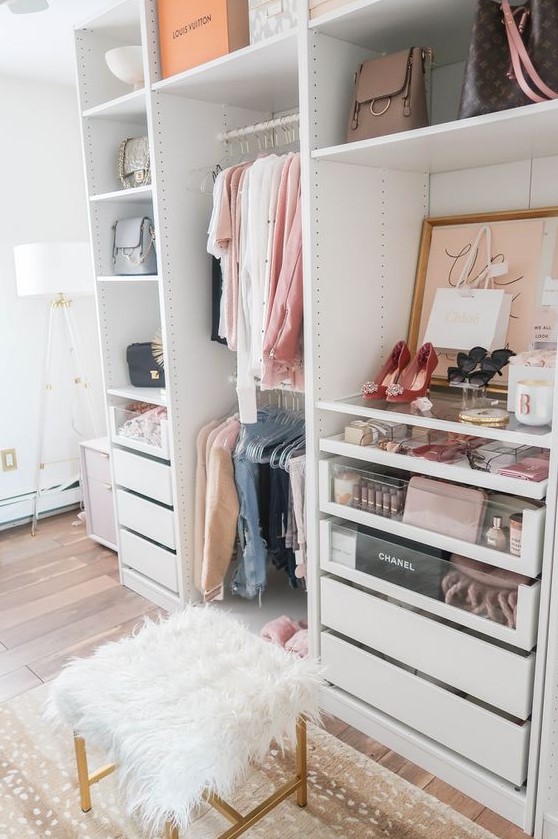 a small glam closet with holders and hangers, built in drawers, open shelving, artworks, a faux fur stool and a printed rug
