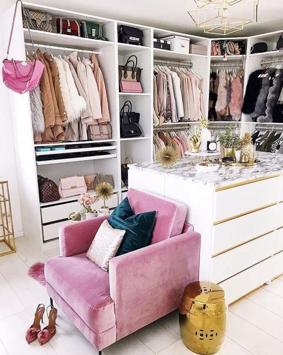 a small glam closet with lots of holders with hangers, shelves and drawers, a large dresser and a pink chair