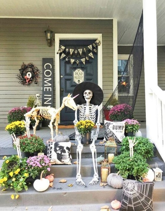 a creative Hallowene porch with a skeleton and a skeleton dog, candle lanterns, blooms and greenery and signs and buntings