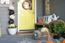 26 a cute and colorful Halloween porch with greenery, blooms, natural pumpkins, a ghost pillow, a buting, a wreath and a stack of pumpkins
