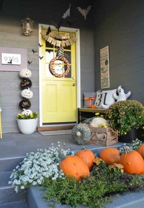 a cute and colorful Halloween porch with greenery, blooms, natural pumpkins, a ghost pillow, a buting, a wreath and a stack of pumpkins