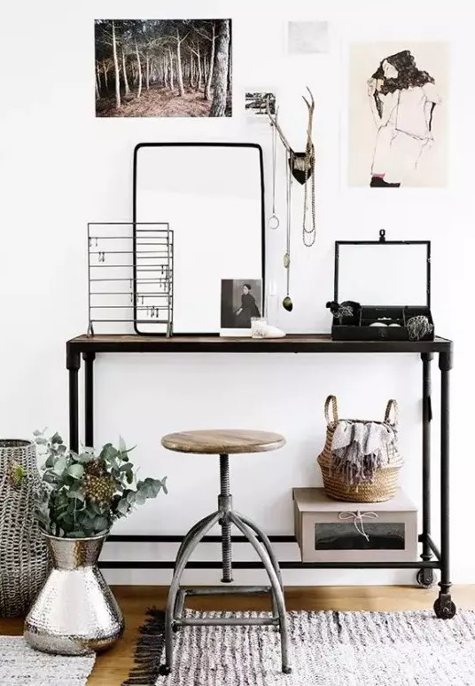 a small and pretty industrial working space with a metal console table, a metal pipe and wood stool, various jewelry on stands and some decor