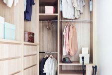 30 a small stylish closet done in light stained wood, with holders for clothes hangers, some open shelves, built-in drawers and a black chair