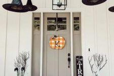 31 a Halloween porch decorated with witches’ hats and legs, branches, pumpkins, hay, blooms and a plaid sign on the door