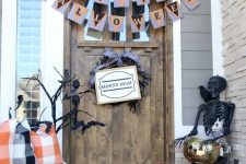 32 a Halloween porch with white and orange pumpkins, candle lanterns, buntings, a black skeleton and black branches plus a twig wreath