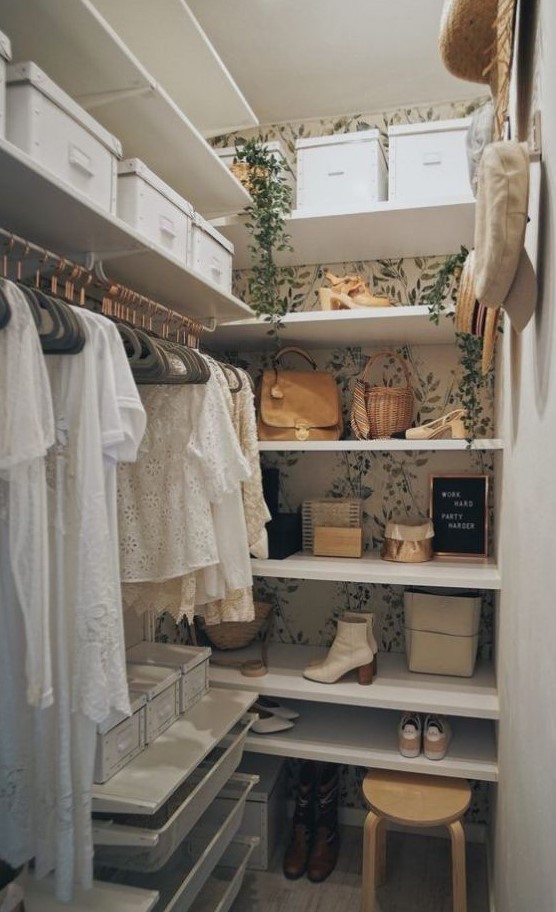 a tiny girlish closet with botanical wallpaper, a faux cascading plant, open shelves, some cubbies, holders for hangers and a wooden stool