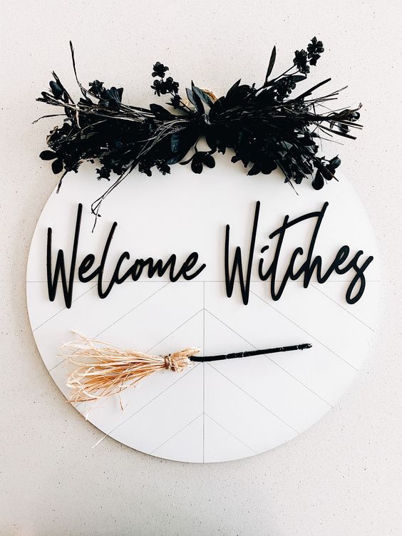a stylish black and white Halloween sign with black faux blooms, black calligraphy and a small broom is cool and fun