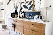 49 chic Halloween console table styling with a sign and an artwork, black plates and branches, a black cauldron and a mirror with a spider