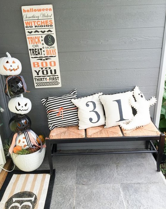 stacked carved pumpkins in a pot, a bench with Halloween pillows, a sign and a mat for Halloween