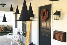 55 witch hats suspended, natural pumpkins, candle lanterns and a bold fall bloom wreath for a Halloween porch