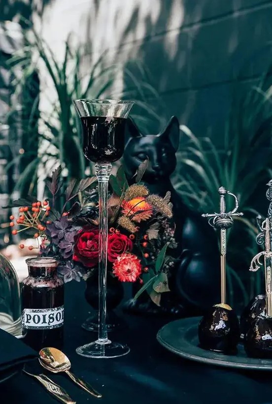 a Halloween tablescape done in black, with a black cat figurine and a bold floral centerpiece with berries and dried touches