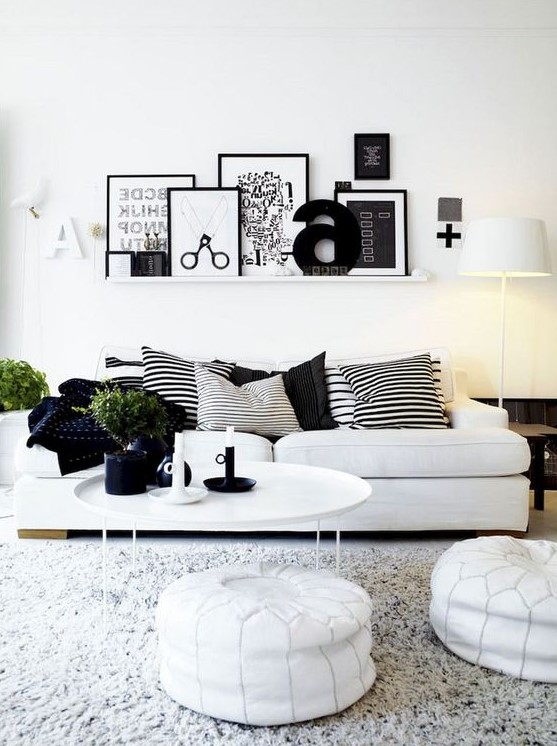 a Nordic living room with a gallery wall on a ledge, a white sofa, leather ottomans and a pack of striped pillows