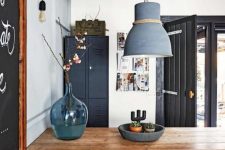 a Scandi industrial dining room with a black storage cabinet, a stained table and mismatching chairs, a grey pendant lamp and bulbs