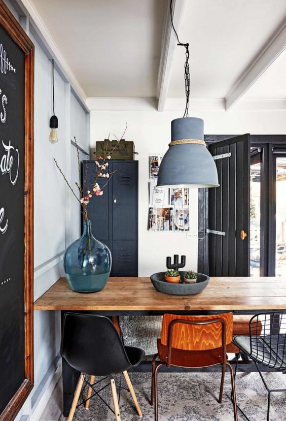 a Scandi industrial dining room with a black storage cabinet, a stained table and mismatching chairs, a grey pendant lamp and bulbs