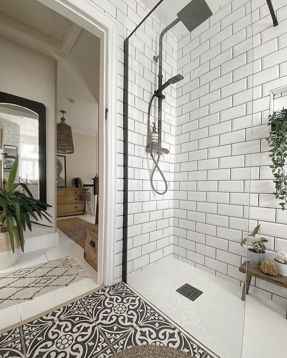 a Scandinavian bathroom with white subway tiles, a black and white floor, a wooden stool and potted plants is a cool space