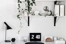 a Scandinavian home office nook with a white desk, a black chair, lamp and some wall-mounted shelves