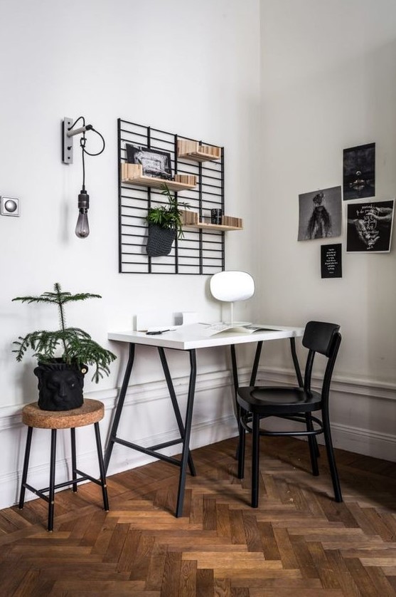 a Scandinavian home office with a white desk, a black chair, a cork stool, a grid with shelves, a black and white gallery wall