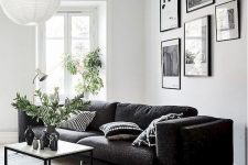 a Scandinavian living room with a black sofa, a small coffee table and a pendant lamp and a gallery wall