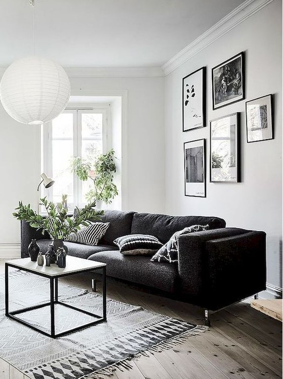 a Scandinavian living room with a black sofa, a small coffee table and a pendant lamp and a gallery wall