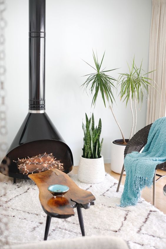 a beautiful and light filled nook with a black Malm fireplace, a black woven chair, a blue blanket and a living edge table