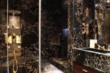 a beautiful black and gold stone tile bathroom with a glass enclosed shower space, a stained vanity and a stone sink and a mirror