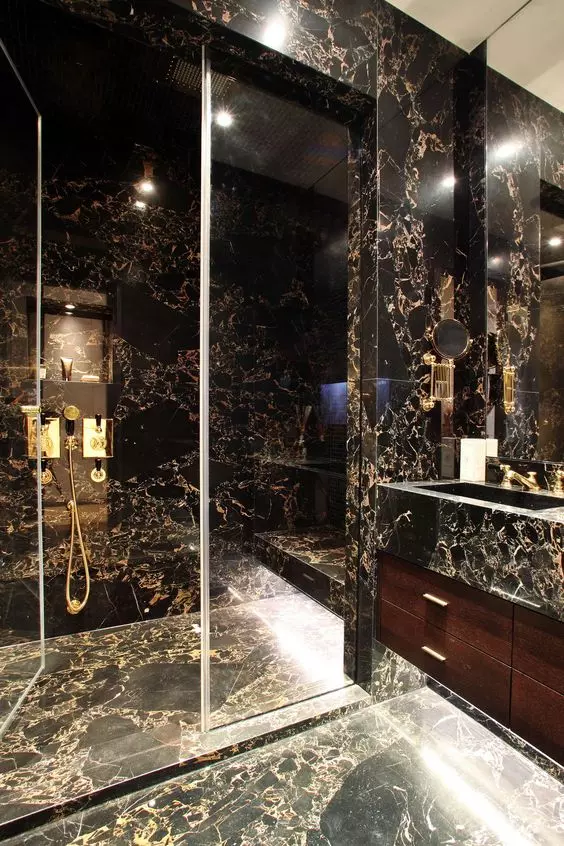 a beautiful black and gold stone tile bathroom with a glass enclosed shower space, a stained vanity and a stone sink and a mirror