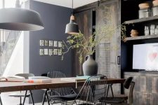 a beautiful rustic industrial dining space with a large table with a wood tabletop, mismatching chairs and stools, black pendant lamps and a reclaimed wood storage unit