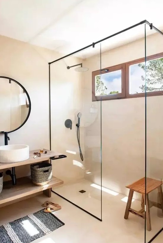 a beige contemporary bathroom with a shower space enclosed in glass, a floating open shelf vanity, a round mirror in a black frame, black fixtures
