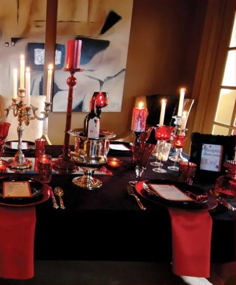 a black and deep red party table with red candles and candle holders, red napkins with a black tablecloth