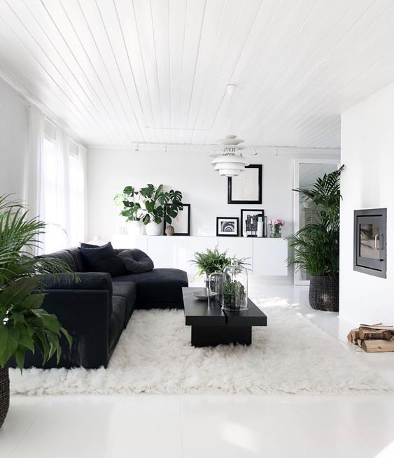 a black and white Scandinavian living room with a built in fireplace, a black sectional, a black coffee table, a floating credenza and potted greenery