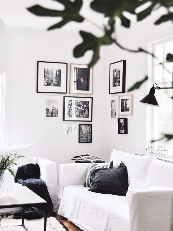 a black and white Scandinavian living room with white seating furniture, a black and white corner gallery wall and greenery