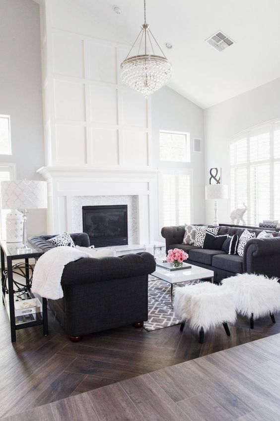 a black and white farmhouse living room with a built-in fireplace, a couple of black sofas, a coffee table and a large crystal chandelier