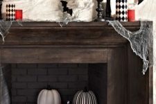 a black, red and white Halloween mantel with painted pumpkins, printed candles, bats and a cat skeleton is amazing