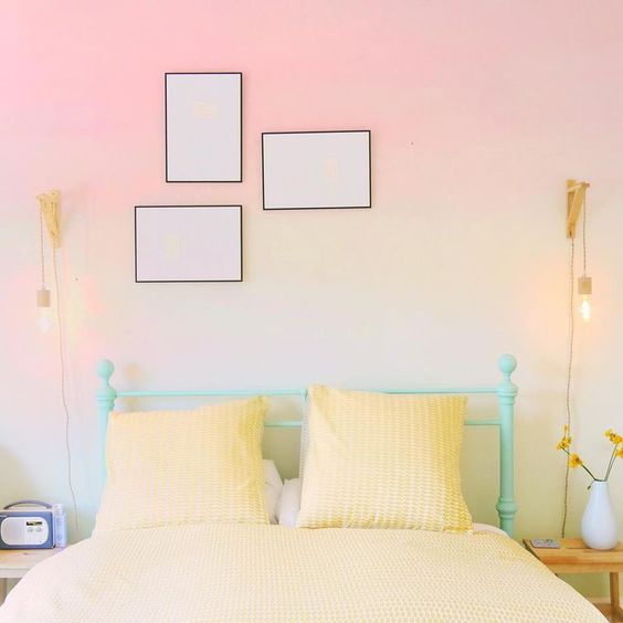 a bold bedroom with gradient walls, a mint green bed with yellow bedding, a mini gallery wall and bright bulbs hanging on both sides of the bed