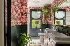 a bold eclectic bathroom with pink wallpaper walls, a stained vanity with two sinks, a bold and colorful rug and potted plants