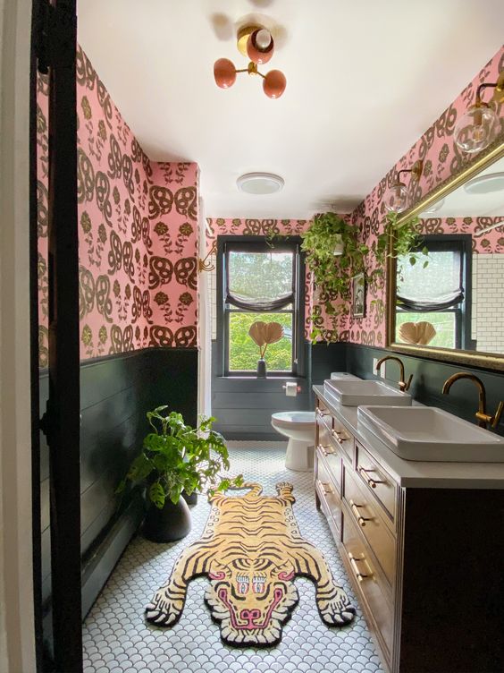 a bold eclectic bathroom with pink wallpaper walls, a stained vanity with two sinks, a bold and colorful rug and potted plants