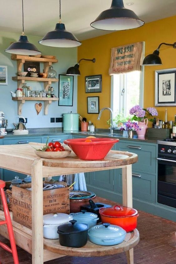 a bold eclectic kitchen with a mustard and blue wall, teal cabinets, grey stone countertops, open shelves, black pendant lamps